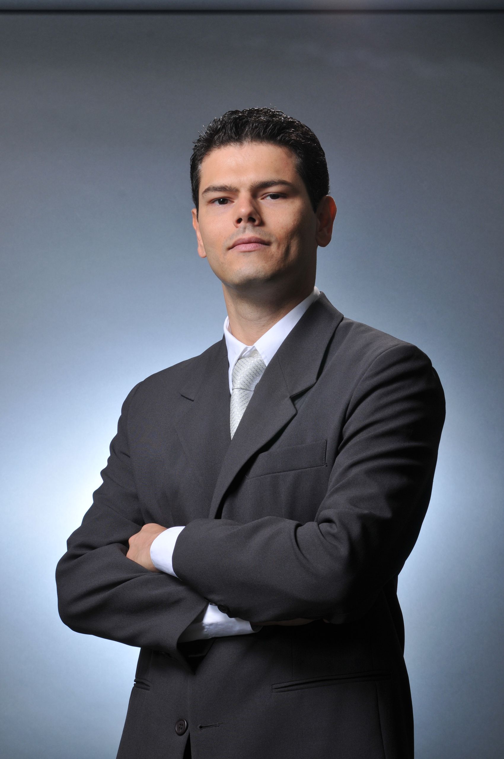 Confident businessman wearing a gray suit with crossed arms. Professional formal portrait.
