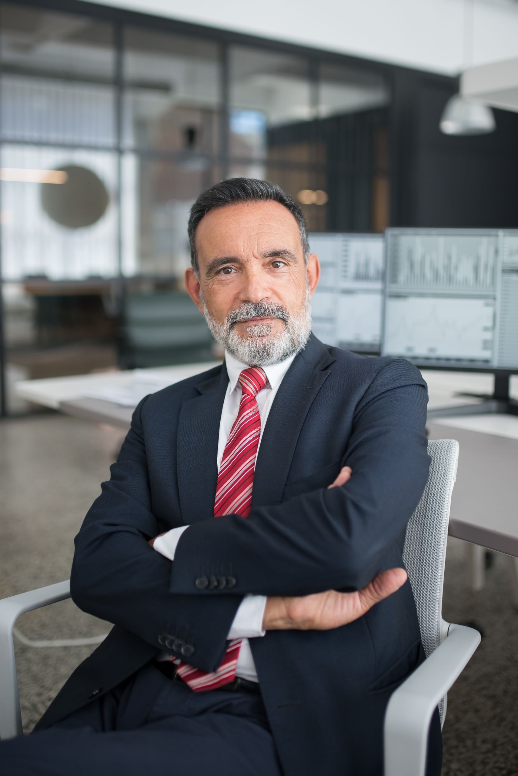 Professional businessman sitting confidently in a modern office with multiple screens displaying data.